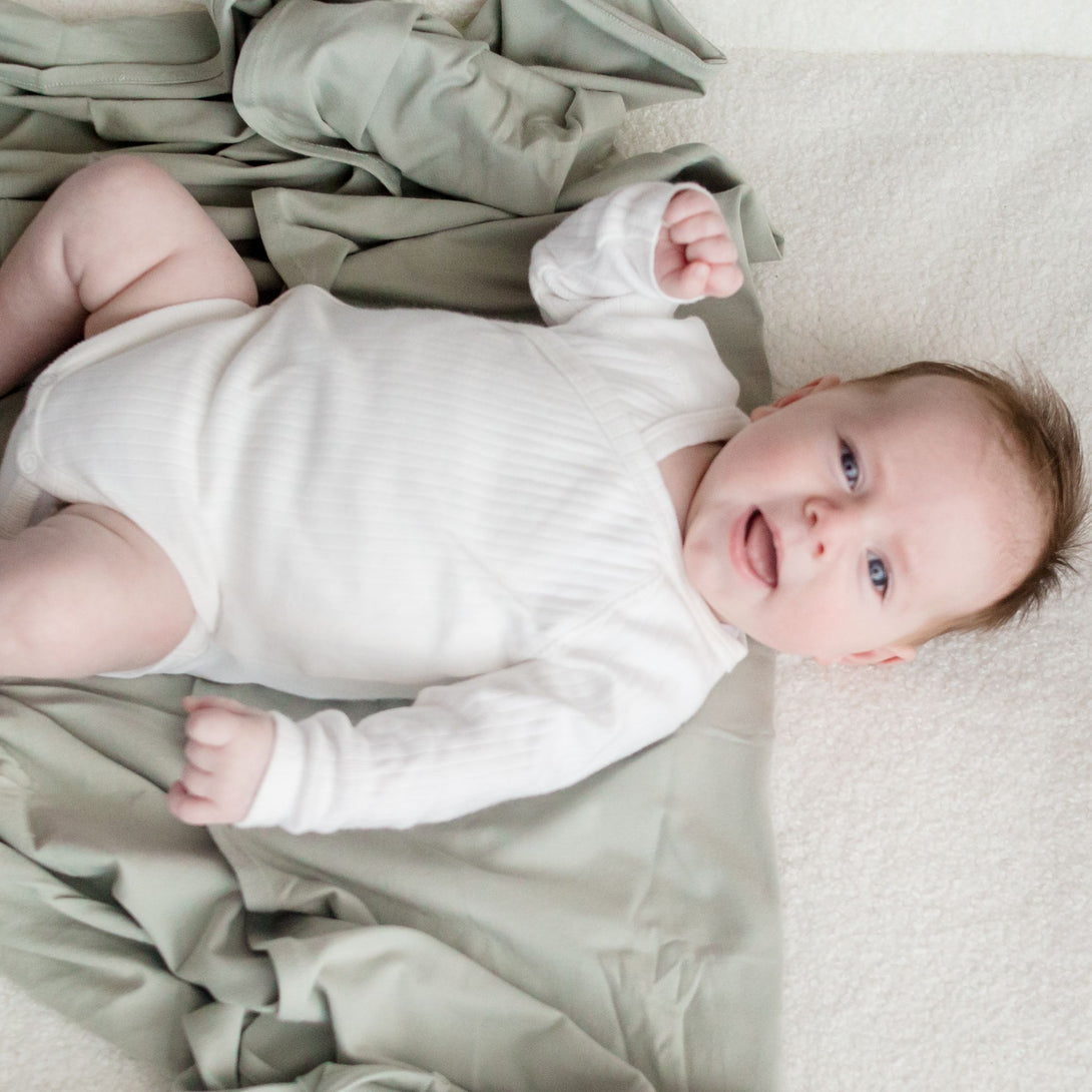 Baby laying on Stretchy Swaddle baby Blanket | Sage Green (Organic)