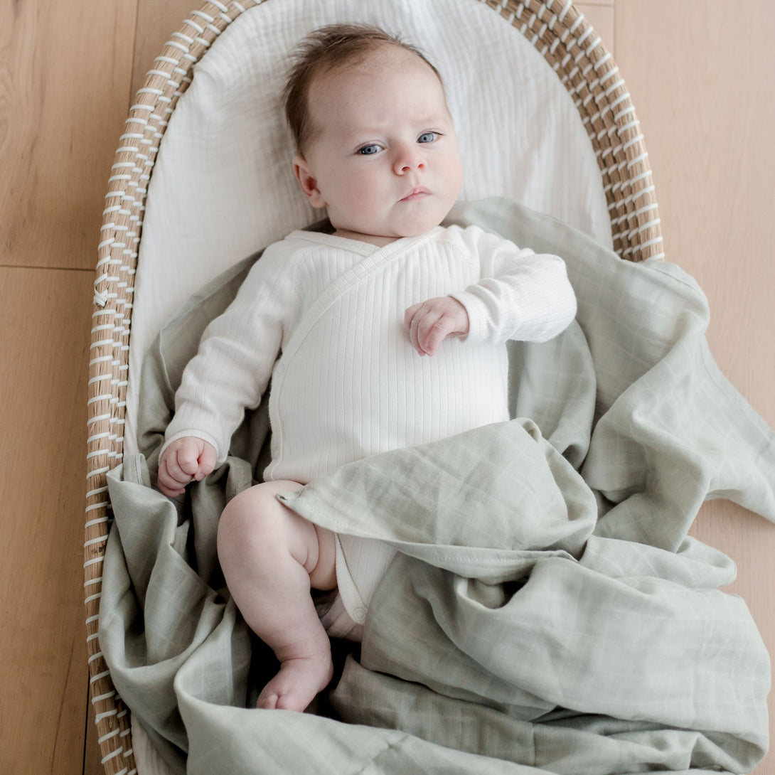 Baby wearing  on Muslin Swaddle Blanket | Sage Green (Organic)