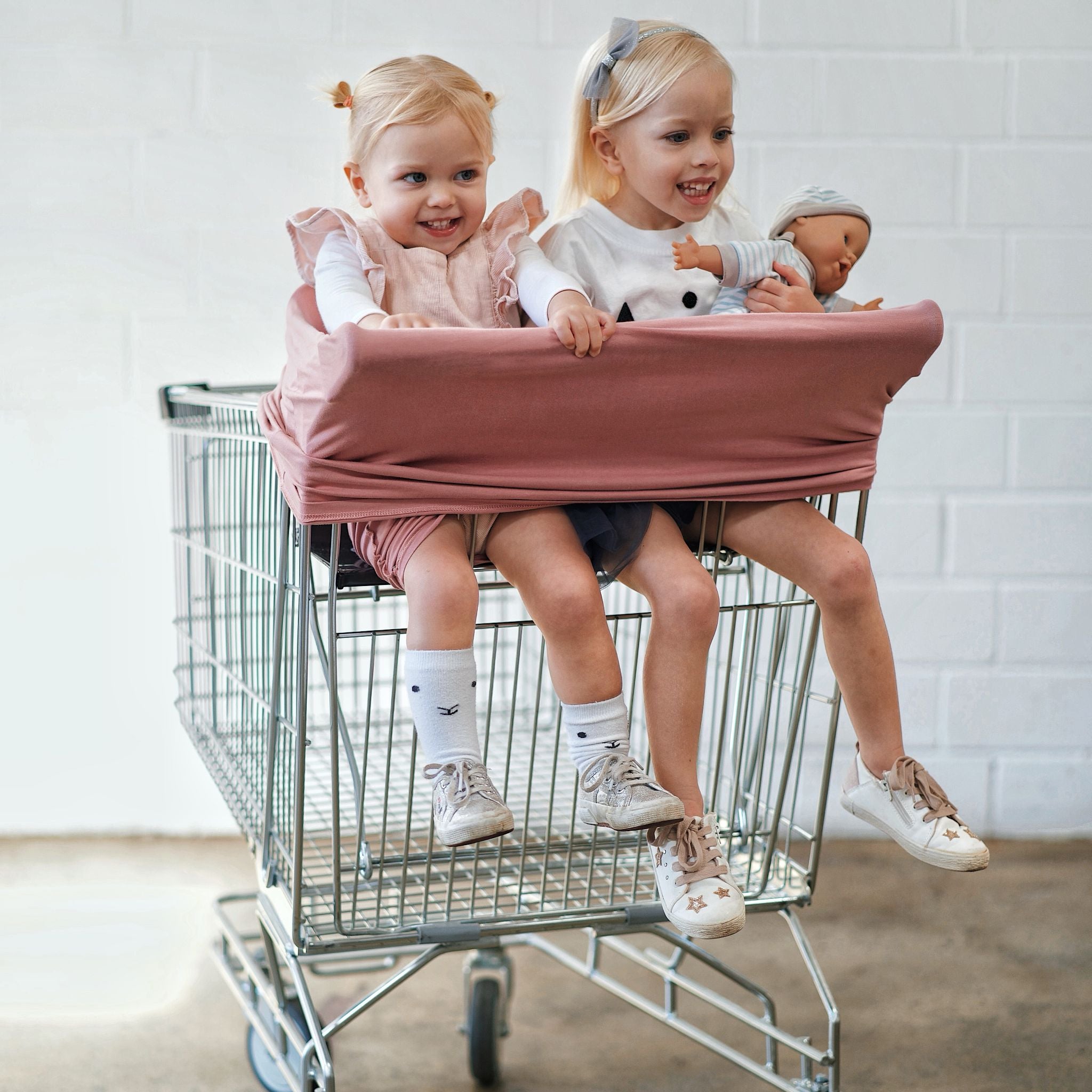 Two babies are sitting in shopping cart wearing  Dusty Rose 5 in 1 mama cover